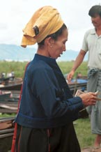 to 30K Jpeg 9809O12 Pa'O woman at Nampan 5-day rotating market, Lake Inle, Shan State. She is paying for her liquid fuel. Note the short serge jacket with details of the fabric woven in the selvedge used to trim the back seam and the edge of the front pocket. She is wearing the jacket over her loose blouse with embroidered seam trimmings. This is then worn over a longyis.