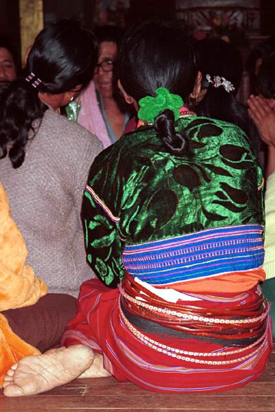 80K Jpeg A Silver Palaung woman in the Buddhist temple at Pein Ne Bin village near Kalaw, northwestern Shan State joining in the prayers on the day after the full moon 'Full Moon Day". She is wearing a traditional hand woven skirt, embroidered shiny velvet blouse and the Silver Palaung identifying bamboo or rattan hoops. There are also glimpses of a white sash and also dark silky threads tied around the waist.