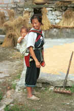 Jpeg 34K Bouyei mother and child pausing in raking the rice outside their home - Bi Ke village, Mi Gu township, Zhenfeng county, Guizhou province 0010r29.jpg