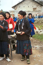 to Jpeg 46K  0110D13 Women offering us alchohol as part of our welcome to Gan He village, Ya Rong township, Huishui county, Guizhou province, south-west China. The people living in this village are known as Qing Miao. There has been much intermarriage between Miao and Bouyei which is evident from the every-day costume of the women. The pieced skirts of applique and wax-resist were originally only worn at funerals but today they are worn for special festivals and dance competitions.