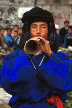 to Jpeg 55K 0110D16  Trumpeter blowing his welcome to Gan He village, Ya Rong township, Huishui county, Guizhou province, south-west China. Note the complex weaving of the ends of his head-cloth. The people living in this village are known as Qing Miao. There has been much intermarriage between Miao and Bouyei which is evident from the costume of the women.