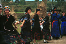 to Jpeg 50K  0110D17  Girls dancing and trumpeters playing as part of our welcome to Gan He village, Ya Rong township, Huishui county, Guizhou province, south-west China. The people living in this village are known as Qing Miao. There has been much intermarriage between Miao and Bouyei which is evident from the every-day costume of the women. The pieced skirts of applique and wax-resist being worn by the girls were originally only worn at funerals but today they are worn for special festivals and dance competitions.