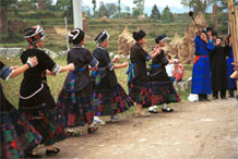 to Jpeg 57K  0110D18A Girls dancing as part of our welcome to Gan He village, Ya Rong township, Huishui county, Guizhou province, south-west China. The people living in this village are known as Qing Miao. There has been much intermarriage between Miao and Bouyei which is evident from the every-day costume of the women. The pieced skirts of applique and wax-resist being worn by the girls were originally only worn at funerals but today they are worn for special festivals and dance competitions.