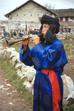 to Jpeg 55K 0110D21  Trumpeter blowing his welcome to Gan He village, Ya Rong township, Huishui county, Guizhou province, south-west China. Note the complex weaving of the ends of his head-cloth. The people living in this village are known as Qing Miao. There has been much intermarriage between Miao and Bouyei which is evident from the costume of the women.