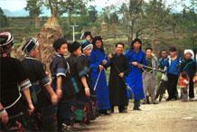 to Jpeg 54K  0110D24 Girls dancing past the trumpeters as part of our welcome to Gan He village, Ya Rong township, Huishui county, Guizhou province, south-west China. The people living in this village are known as Qing Miao. There has been much intermarriage between Miao and Bouyei which is evident from the every-day costume of the women. The pieced skirts of applique and wax-resist being worn by the girls were originally only worn at funerals but today they are worn for special festivals and dance competitions.