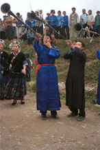 toJpeg 52K  0110D28 Girls dancing and very long and loud trumpets being played as part of our welcome to Gan He village, Ya Rong township, Huishui county, Guizhou province, south-west China. The people living in this village are known as Qing Miao. There has been much intermarriage between Miao and Bouyei which is evident from the every-day costume of the women. The pieced skirts of applique and wax-resist being worn by the girls were originally only worn at funerals but today they are worn for special festivals and dance competitions.