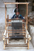 to Jpeg 56K 0110E02  Woman weaving an indigo plaid fabric on an upright heddle loom in Gan He village, Ya Rong township, Huishui county, Guizhou province, south-west China. The people living in this village are known as Qing Miao. There has been considerable intermarriage between Miao and Bouyei and the costume is very mixed.