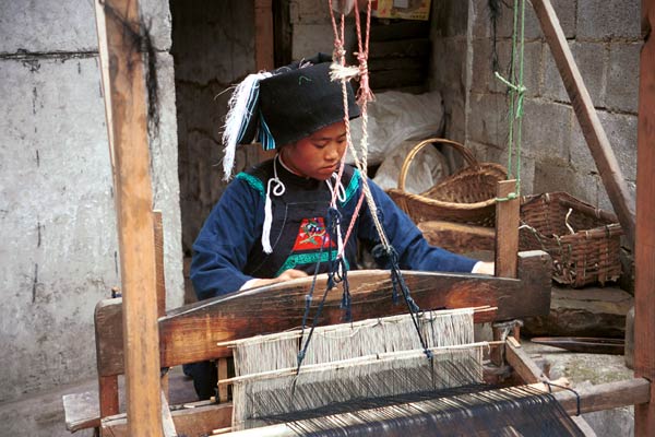 Jpeg 53K  0110E06   Woman weaving an indigo plaid fabric on an upright heddle loom in Gan He village, Ya Rong township, Huishui county, Guizhou province, south-west China. The people living in this village are known as Qing Miao. There has been considerable intermarriage between Miao and Bouyei and the costume is very mixed.