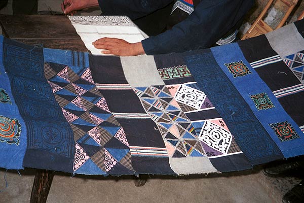 Jpeg 57K  0110E22 A length of pieced fabric ready to be made up into a skirt. Note the wax resist in two shades of indigo, embroidered work and applied plaid triangles of cloth, Gan He village, Ya Rong township, Huishui county, Guizhou province. This is a Qing Miao (or Bouyei/Miao as there has been much intermarriage and the costume is very mixed). 