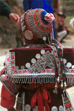 to Jpeg 141K Iron beating Miao festival costume in miniature worn by one of little girls who danced for us in Gao Zhai village, Bai Jin township, Huishui county, Guizhou province. She is wearing what looks like a very ornate baby carrier on her back. Note the finely gathered hat crown worn by the little girl and shown in closeup in photos further down in the photo gallery. I bought one of these beautifully made hats for my collection 0110C23