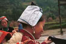 to Jpeg 38K 0111F31 Gejia woman carrying her baby on her back and showing her headdress. The fabric is a machine printed reproduction of a traditional Gejia wax resist design. All the women in this village seemed to be wearing the commercially printed fabric and we did not see any original wax resist being worn on headdresses. Ma Tang village, Kaili City, Guizhou province. 