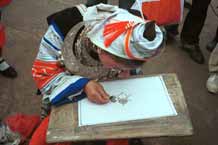 to Jpeg 59K 0111G01 Gejia woman in full festival finery demonstrating wax resist. The fabric on her own costume is commercially printed with traditional Gejia designs and not waxed. Ma Tang village, Kaili City, Guizhou province.