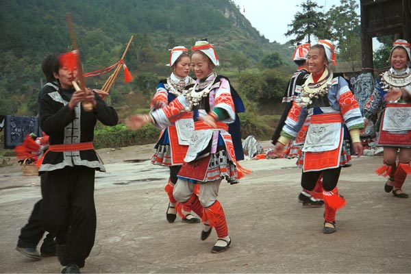 Jpeg 58K 0111G15A Gejia dance troupe performing in Ma Tang village, Kaili City, Guizhou province in November 2001. The apparently wax resist fabric in their costume - at least the headdress, apron and sleeves of the blouse - are now generally made from commercially printed fabric which imitates the Gejia traditional wax resist designs. 