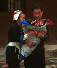 to Jpeg 53K 0111G28 A Gejia couple loving their baby which is wrapped in a winter wax resist baby carrier. Ma Tang village, Kaili City, Guizhou province. 