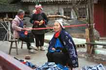 to Jpeg 58K 0111G35 Gejia women weaving braids, knitting hairnets and sewing by a heap of wax resist clothing.  Ma Tang village, Kaili City, Guizhou province.