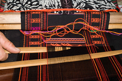 Weaver Huang Ji Xiang, who is a member of the Qi subgroup of the Li people, making the cloth that is called "Li brocade" locally. Weaving proceeds via two separate sheds. After adding a row of ground weft the weaver switches attention to the upper shed where the pattern is formed. She first selects the region of interest with the light colored wooden pick at the bottom of the photo, then uses a second pick to select the warps for the supplementary weft.