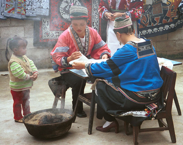 Jpeg 96K Two Miao women wearing their festival costumes setting up their wax resist (batik). Note in the background the wax resist that they are doing for commercial sale. Lou Jia Zhuang village, Anshun city, Guizhou province 0110B17