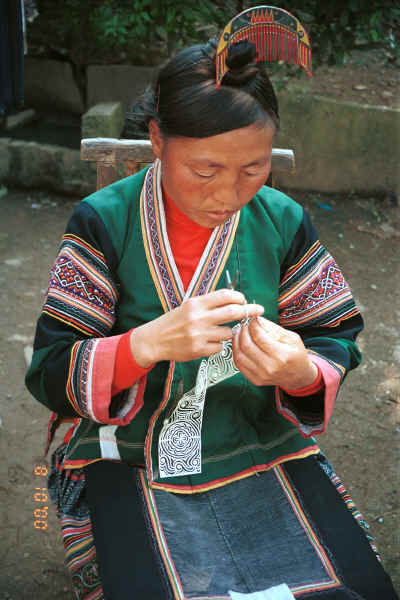 Side Comb Miao married woman finishing off a paper cut-out for embroidery probably for a sleeve insert - Pao Ma Cheng village, Teng Jiao township, Xingren country, Guizhou province 0010n27.jpg