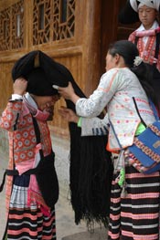 to Jpeg 61K Dressing the hair of a Long Horned Miao girl in festival dress by winding the girl's own hair, wool and perhaps inherited hair around the wooden 'horn'.