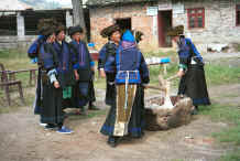 Jpeg 41K Black Miao women kneading stick rice served for festivals.  Note the young women with their heavy earings held by braid and the older women wearing them in pierced earlobes.  The gentian violet dyed back apron and the small insets of gentian dyed silk satin around the embroidered back panel of the jacket are clearly visible.  Zuo Qi village, Min Gu township, Zhenfeng county, Guizhou province 0010q04.jpg