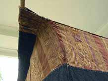 to Jpeg 52K Top corrner hanging detail of Tai Daeng Mosquito Net (pha mung) from Xam Tai in northeast Laos. Approximately: 61" x 65" on the sides and 60" high; hanging pockets extends 4" from main 'box'. Four panels on each side of handspun, handwoven indigo cotton, with silk and cotton heading border in good condition; top of four panels (one is pieced making three parts) gold-colored handspun, handwoven cotton. One side (side 'd') has a panel replaced, or of darker color indigo. Several patches and some holes, although none are larger than 1". A few patches of supplementary warp scraps. All handstitched. Early 20th century.