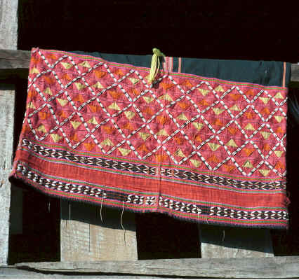 A Sgaw Karen traditional woman's blouse hanging out to dry showing at the bottom the koh dyed (red) cotton embroidery and added Jacob's seeds on the indigo dyed, hand woven base 8812o35A.jpg