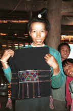 to Jpeg 29K Black Thai woman showing a head cloth which she embroidered several years before - the style has less ornate edging than ones being made and worn today.  Note that, inside the house, she is not wearing a head cloth but showing her hair knot secured by a silver coloured coin fastening.  This is the lady who was demonstrating weaving in the loom above for which we went to a neighbour's house as this Black Thai lady did not have a loom currently set up in her house.  The lady of the house - shown in the photo to the right of this one with a more modern head cloth - was out collecting wood for her cooking fire when we first arrived at her home and watched the weaving.  Both head cloths are now in my collection purchased by way of thanks and in memory of these ladies' kind and generous hospitality. Dien Bien Phu, Lai Chau Province. 9510D27.JPG