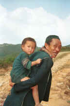 to Jpeg 30K Black Hmong man with a young girl - probably his granddaughter - on his back, in the hills around Sa Pa, Lao Cai Province.  Note the beautifully embroidered collar back on his sleeveless indigo dyed jacket. 9510K13.JPG