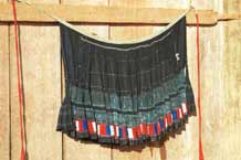 to Jpeg 35 K 9510G19 Flowery Hmong woman's short pleated skirt hanging out to dry outside a house in small road-side village near Phong Tho (Phong Thanh) in Lai Chau Province. The skirt is dyed a dark indigo after very many dippings in the dye vat.  Note the inserted strip of wax resist fabric and the strip of pieced red, blue and white fabric squares from purchased fabric