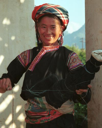 Jpeg 30K 9510G26  Flowery Hmong woman untieing a pleated skirt which has been rolled to keep the pleats in place.  It is just possible to see what is probably and insert of batik in the skirt. Note her blouse with applique and embroidery.  Outside a house in small road-side village near Phong Tho (Phong Thanh) in Lai Chau Province.