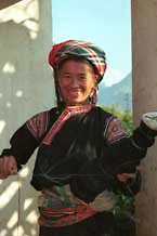 to Jpeg 30K 9510G26  Flowery Hmong woman untieing a pleated skirt which has been rolled to keep the pleats in place.  It is just possible to see what is probably and insert of batik in the skirt. Note her blouse with applique and embroidery.  Outside a house in small road-side village near Phong Tho (Phong Thanh) in Lai Chau Province.