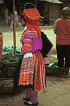 Jpeg 45K 9510K27  Brightly dressed Flowery Hmong woman at a shop stall in Sa Pa, Lao Cai Province.  She is a visitor to Sa Pa, in the town on a training programme, and lives near the Chinese border. The Flowery Hmong near to the border tend to wear more bought trimmings on their clothing which they obtain from China.  Note her embroidered and applique leg wrappings and her long apron.  She only very narrow bands of wax resist on her skirt which features applied strips of fabric and embroidery. 