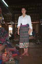 to Jpeg 48K An old Thai minority woven sarong being modeled by a Thai girl in a village West of Hanoi, Vietnam.  The sarong is now in my collection.  See the old lady in the background winding bobbins ready for weaving.  In the foreground is a pile of woven lengths from various families in the village ready for sale. 9510A14T